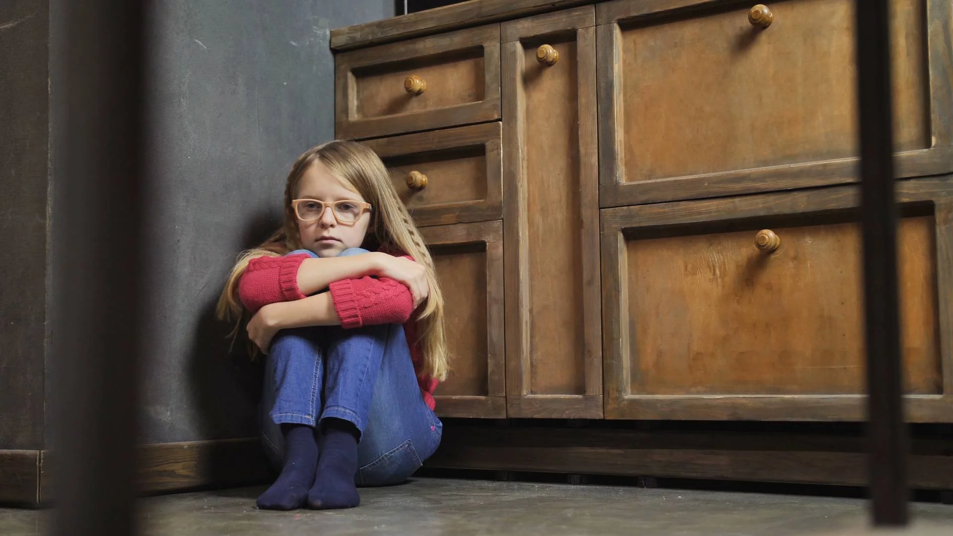 smutna przestraszona dziewczynka siedzi w kącie na podłodze przy komodzie smutna przestraszona dziewczynka siedzi w kącie na podłodze przy komodzie