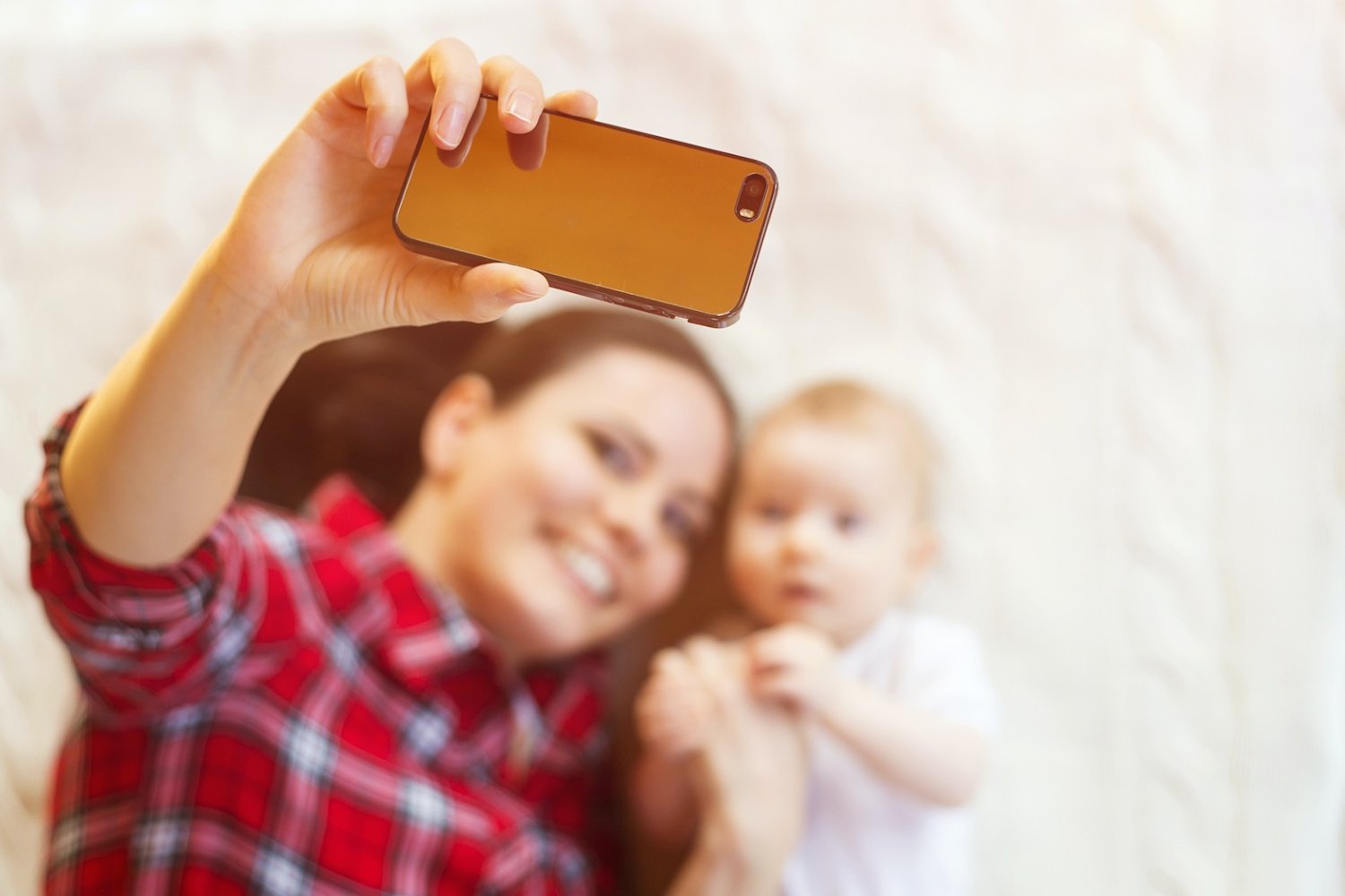 Trendy rodzicielskie, które powinniśmy pożegnać w 2026 roku Na zdjęciu mama robi sobie zdjęcie z dzieckiem (niemowlakiem leżącym na łóżku)