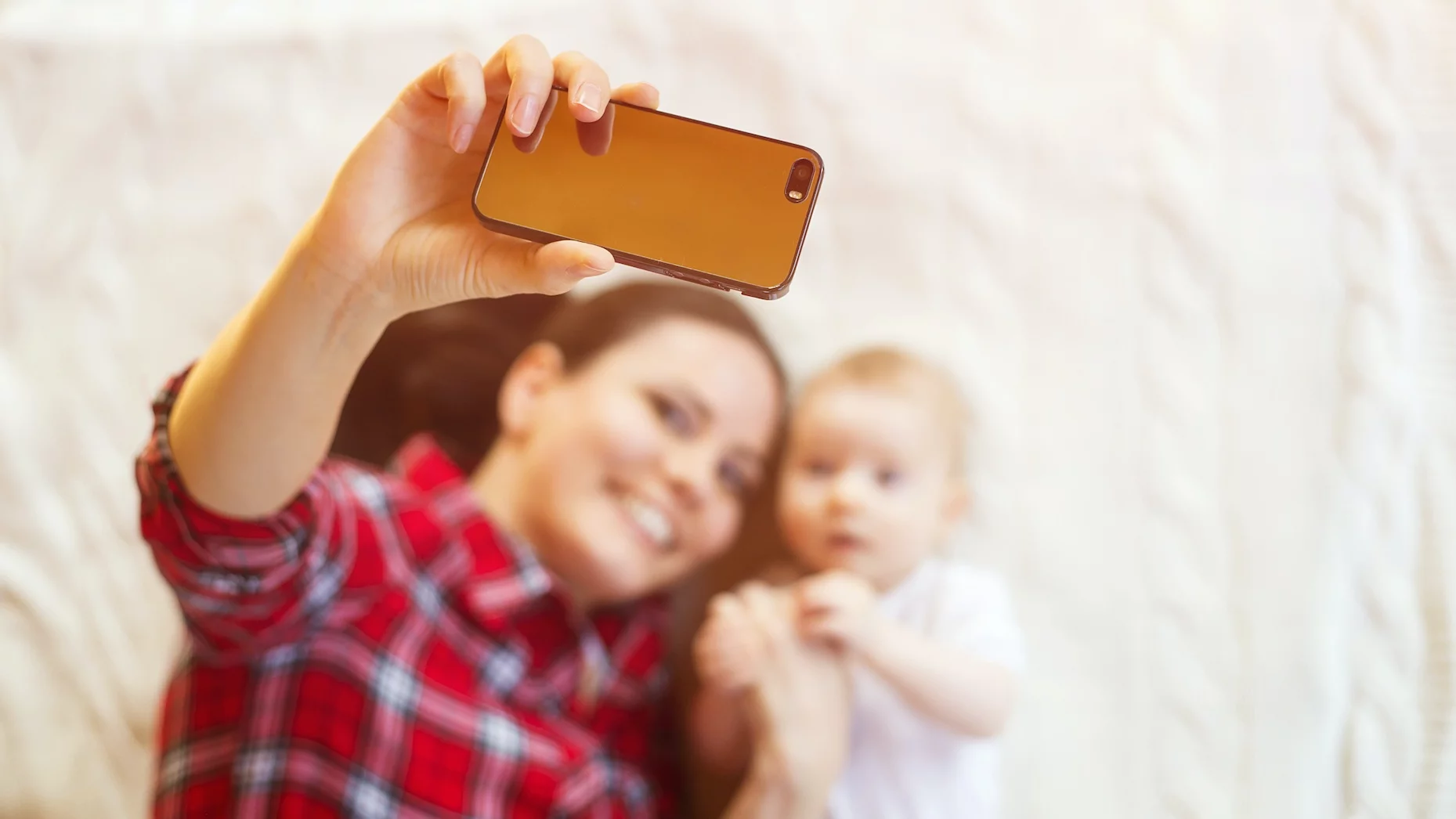 Trendy rodzicielskie, które powinniśmy pożegnać w 2026 roku Na zdjęciu mama robi sobie zdjęcie z dzieckiem (niemowlakiem leżącym na łóżku)