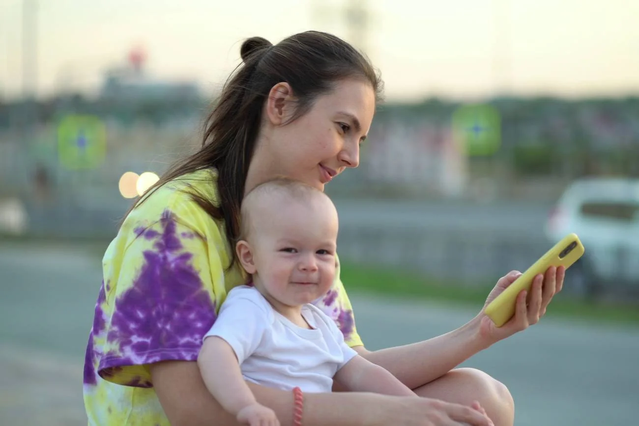 mama patrzy w smartfona, trzymając na rękach dziecko
