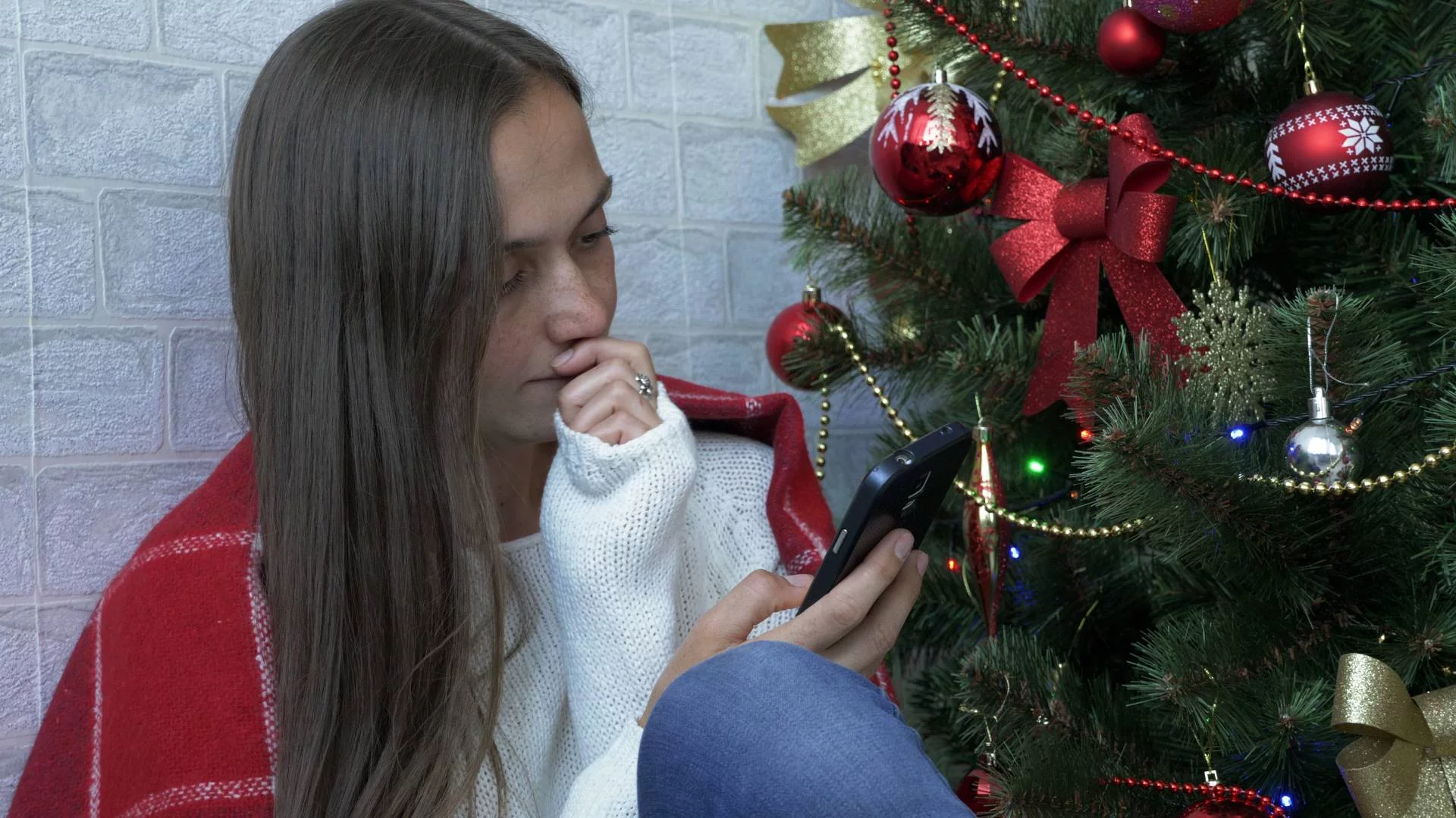 kobieta siedzi przy choince i scrolluje ekran