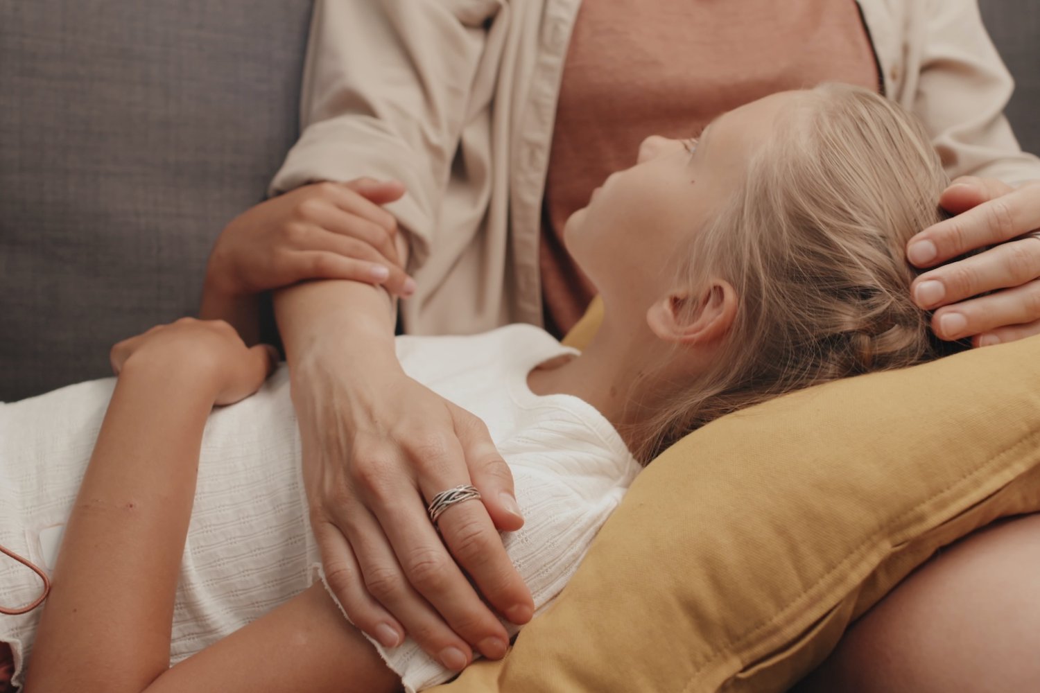 Na zdjęciu jest mama z dziewczynką. Córka opiera głowę o kolana mamy i słucha co ona do niej mówi.