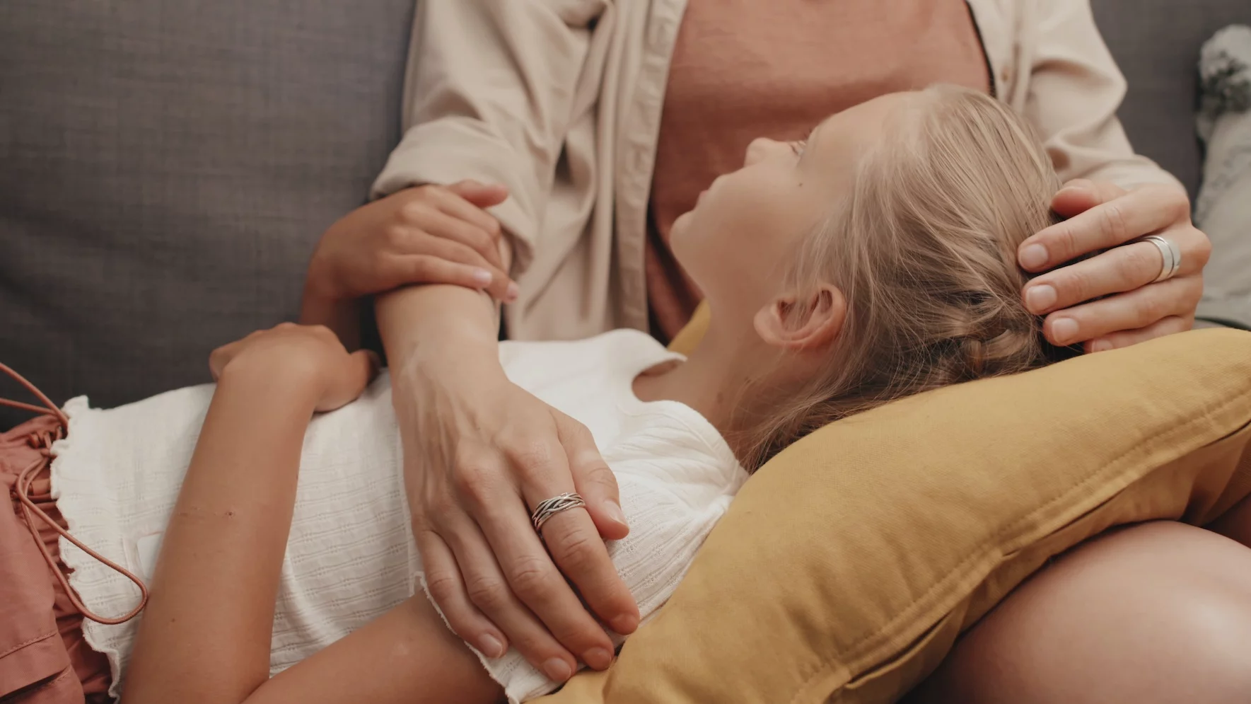 Na zdjęciu jest mama z dziewczynką. Córka opiera głowę o kolana mamy i słucha co ona do niej mówi.