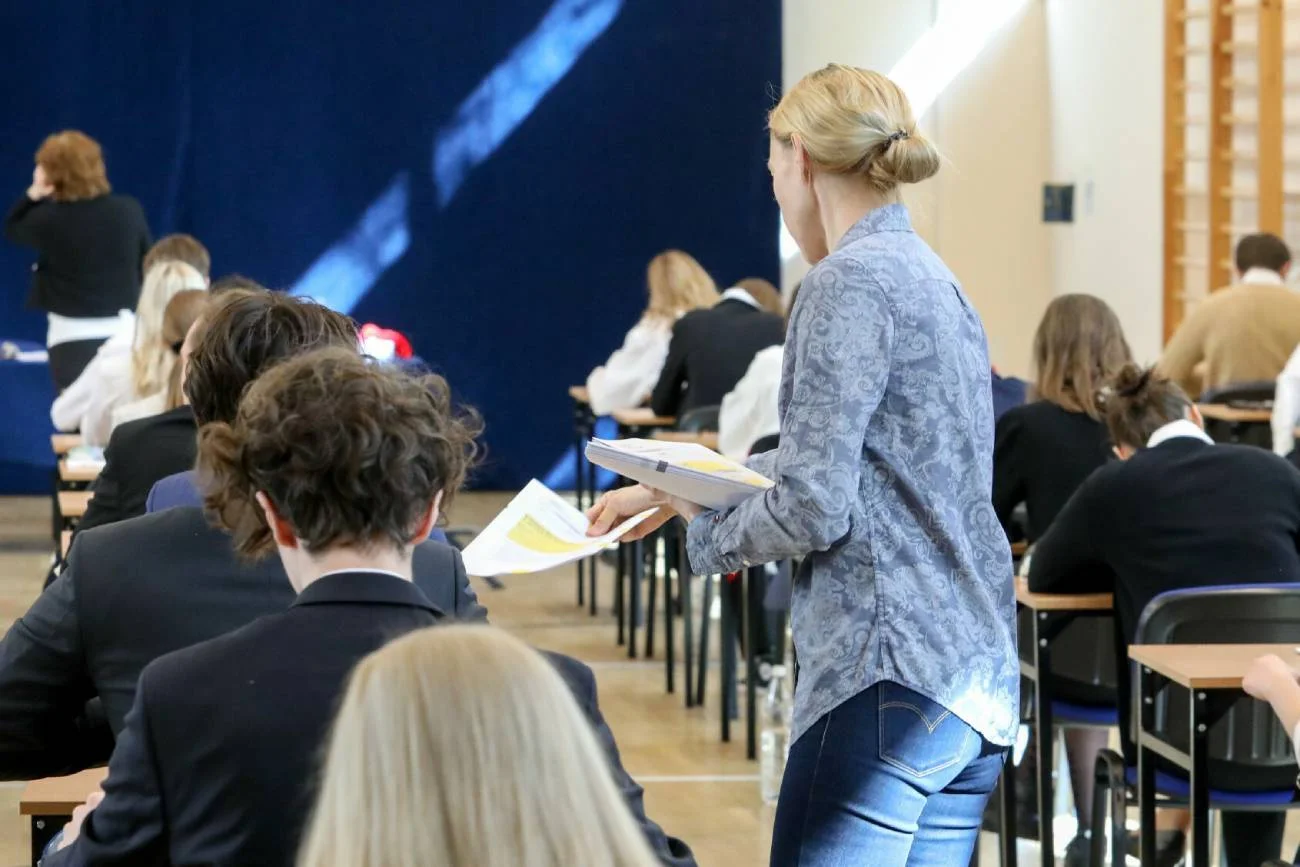 Uczniowie piszą egzamin maturalny na sali gimnastycznej.
