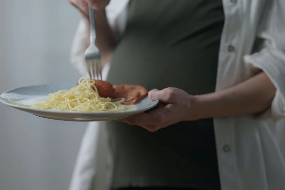 Tych produktów nie wolno jeść w ciąży. Lista zakazanych rzeczy Na zdjęciu widać ciężarną kobietę, która trzyma talerz z obiadem