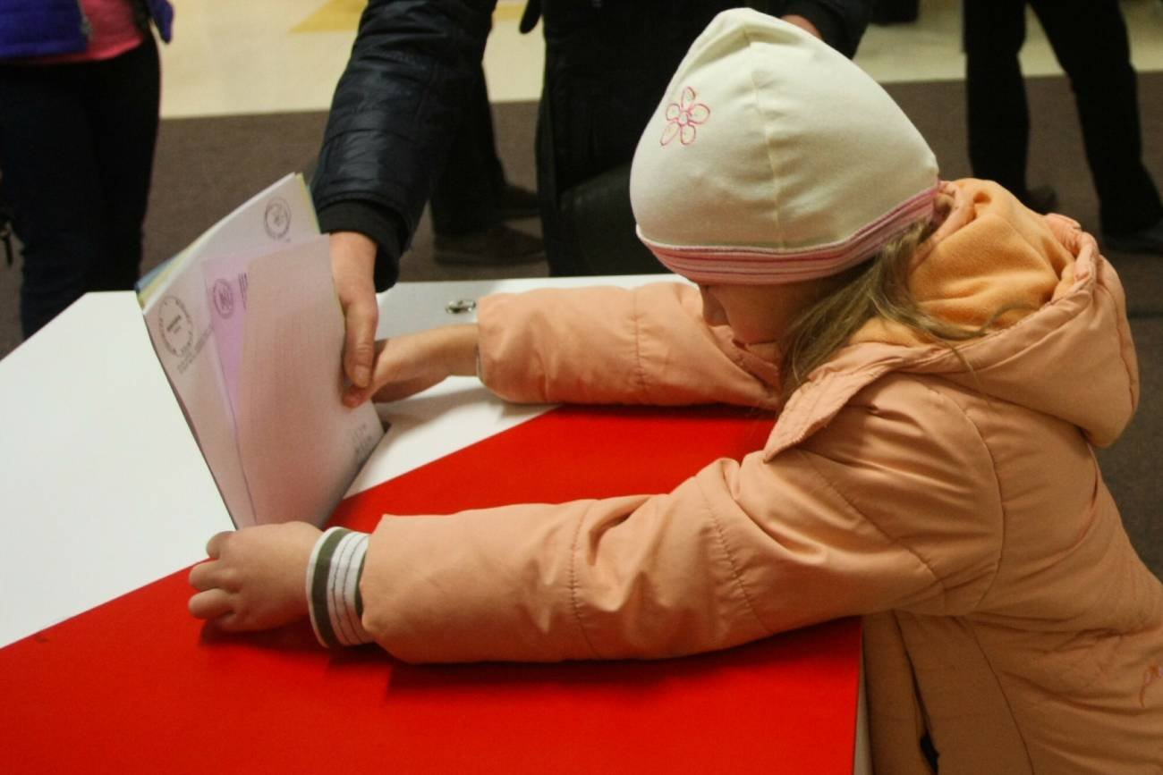 Mała dziewczynka wrzuca karty wyborcze do urny podczas wyborów.