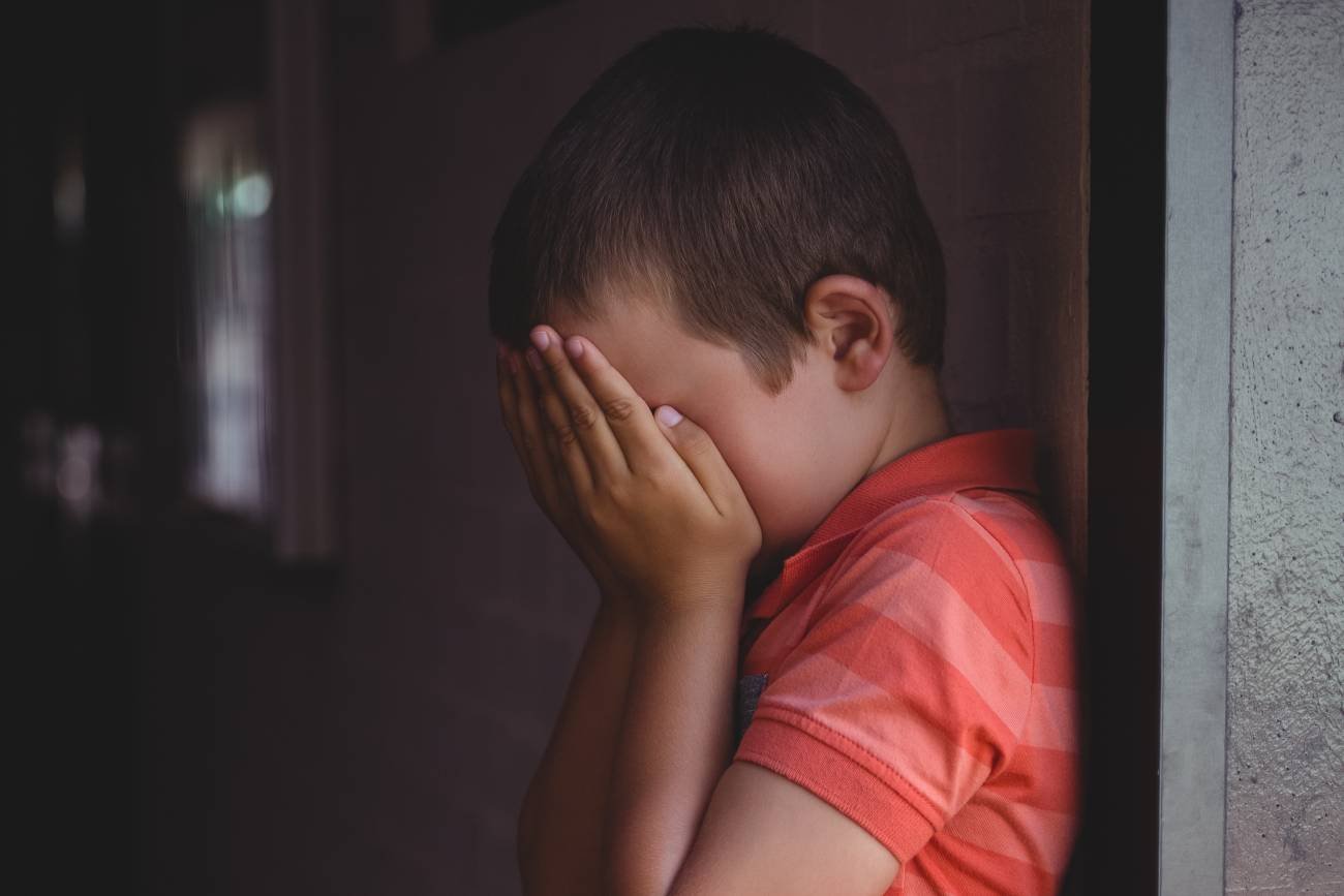 Mały zasmucony chłopiec ze spuszczoną głową.