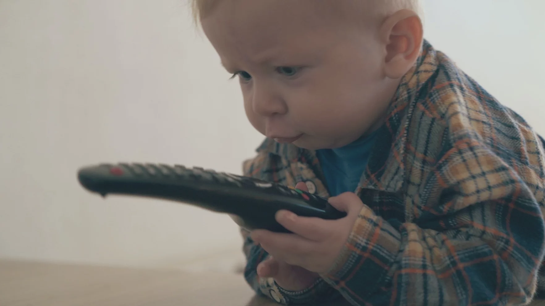 Telewizor włączony w tle szkodzi dziecku. Na zdjęciu widać niemowlaka trzymającego pilota od telewizora.