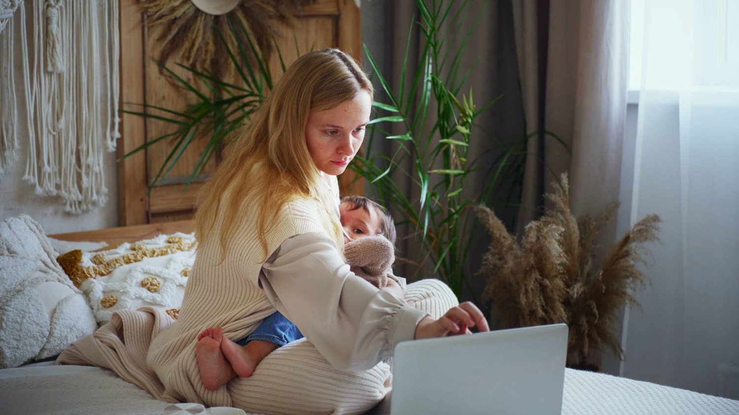 mama karmi dziecko piersią i pracuje przy laptopie