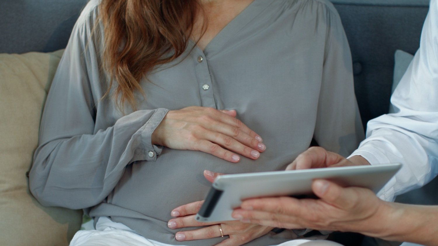 Na zdjęciu jest ciężarna, której ktoś pokazuje tablet