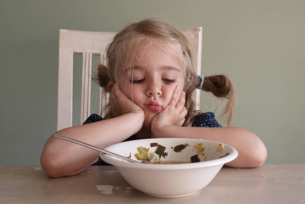 Mała dziewczynka przy stole niechętnie patrzy na obiad.
