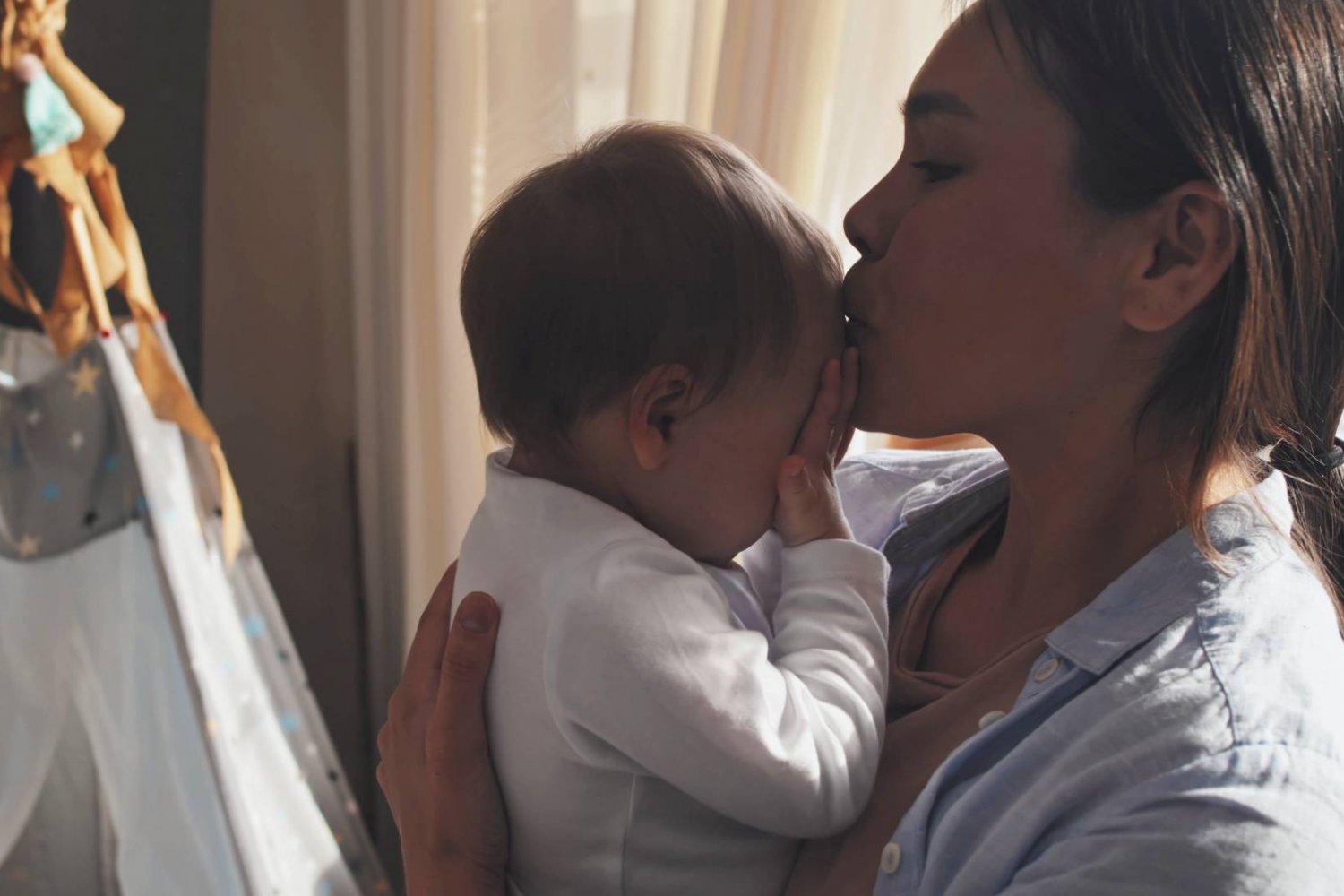 młoda mama trzyma na rękach niemowlaka i całuje go w główkę młoda mama trzyma na rękach niemowlaka i całuje go w główkę