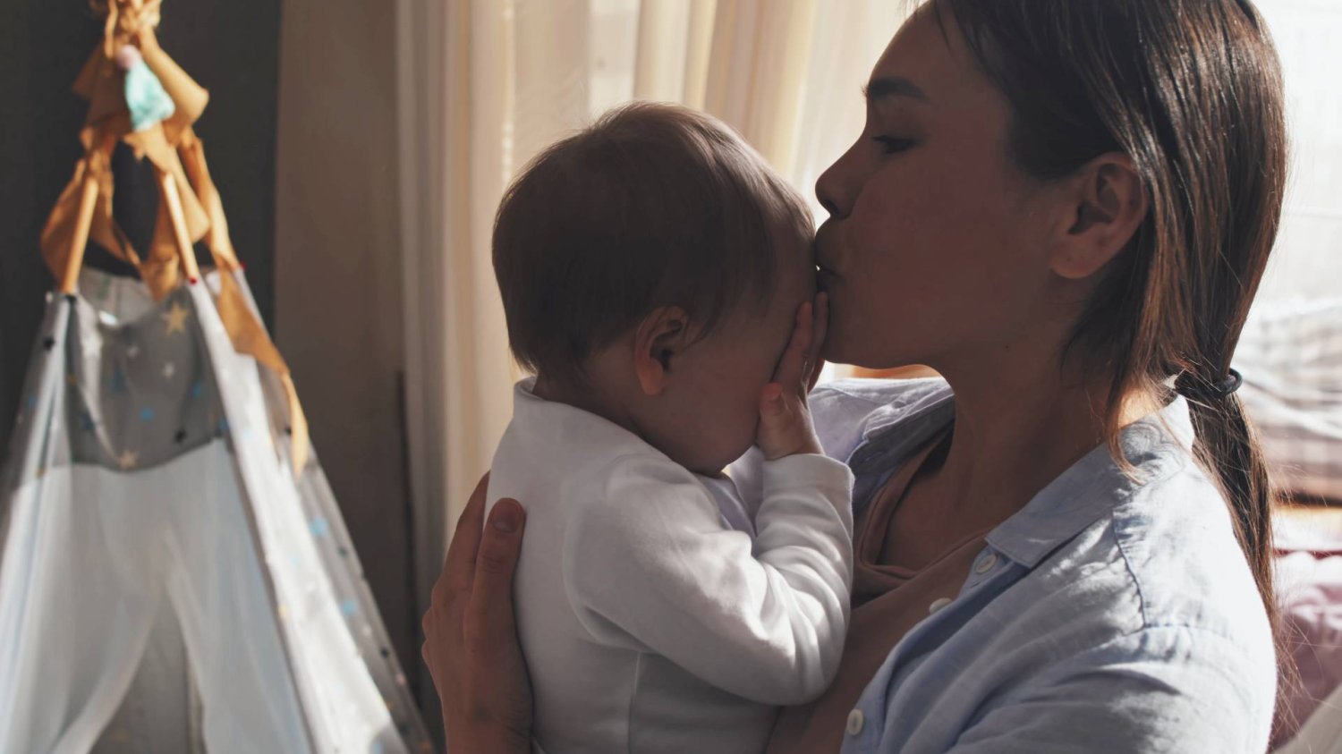 młoda mama trzyma na rękach niemowlaka i całuje go w główkę młoda mama trzyma na rękach niemowlaka i całuje go w główkę