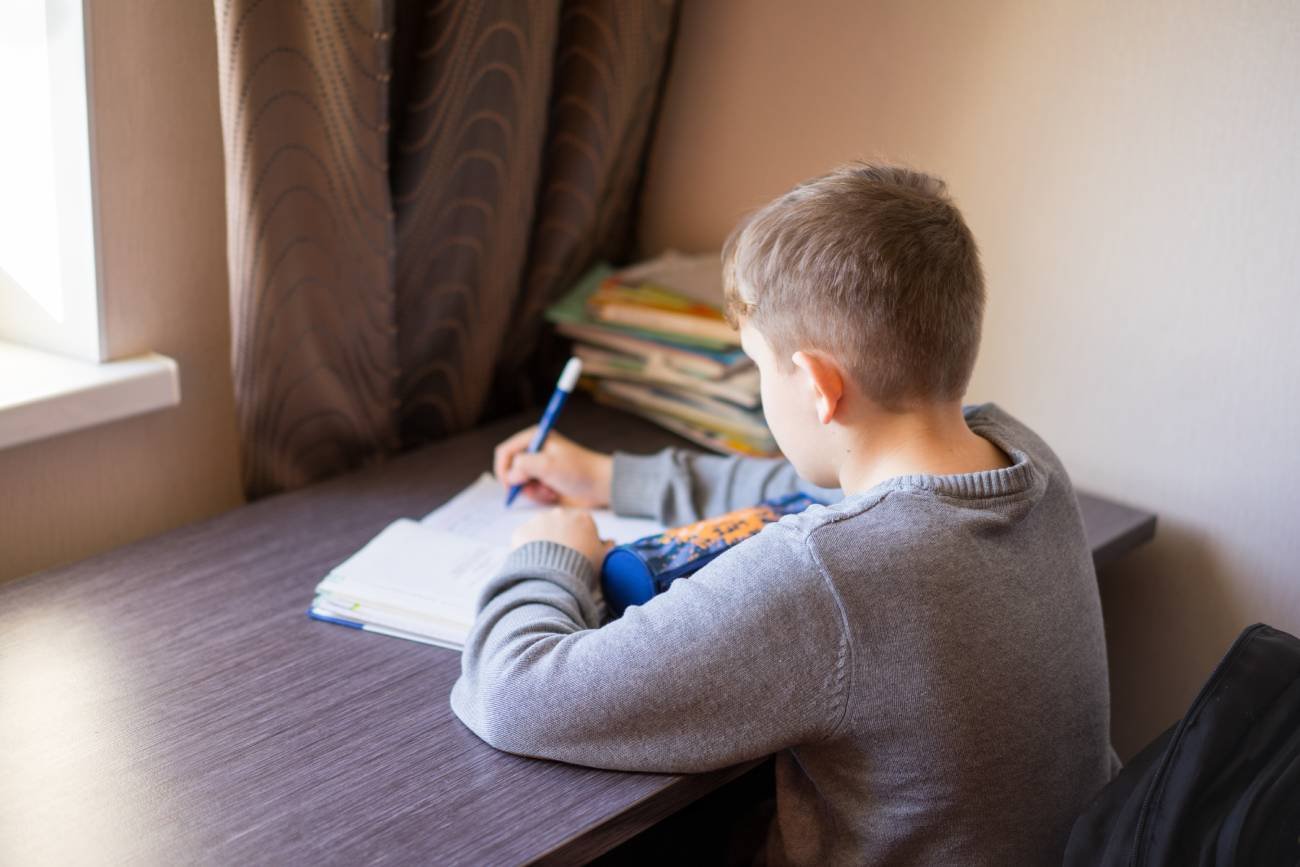 Chłopiec odrabia przy biurku pracę domową.