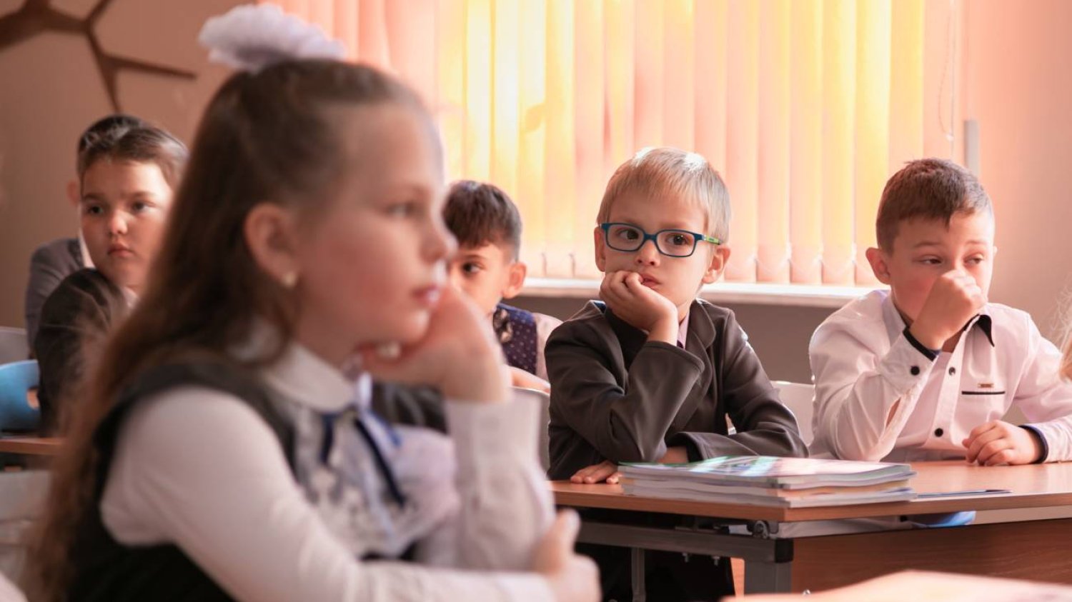 Dzieci siedzą na lekcji w ławkach i słuchają nauczyciela.