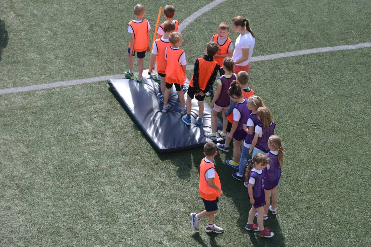 Dzieci na lekcji WF-u ćwiczą i grają w gry sportowe w pełnym słońcu.