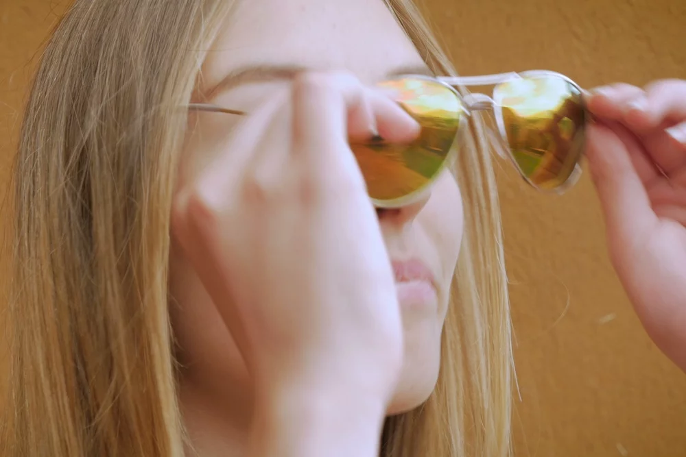 Niektóre elementy garderoby możesz śmiało dzielić ze swoją nastoletnią córką. Na zdjęciu widać kobietę zakładającą okulary pilotki