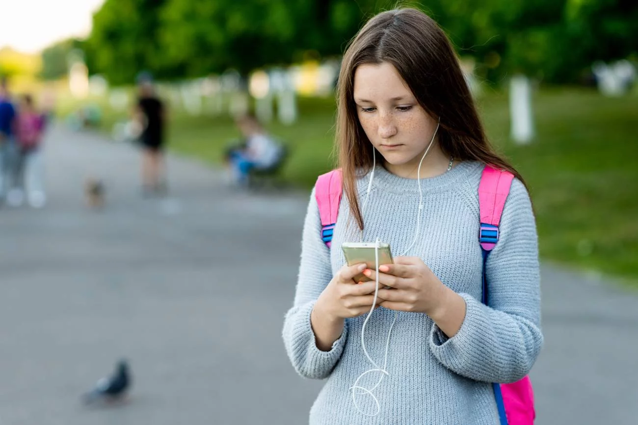 Nastolatka patrzy się w ekran telefonu i scrolluje tablicę w social mediach.