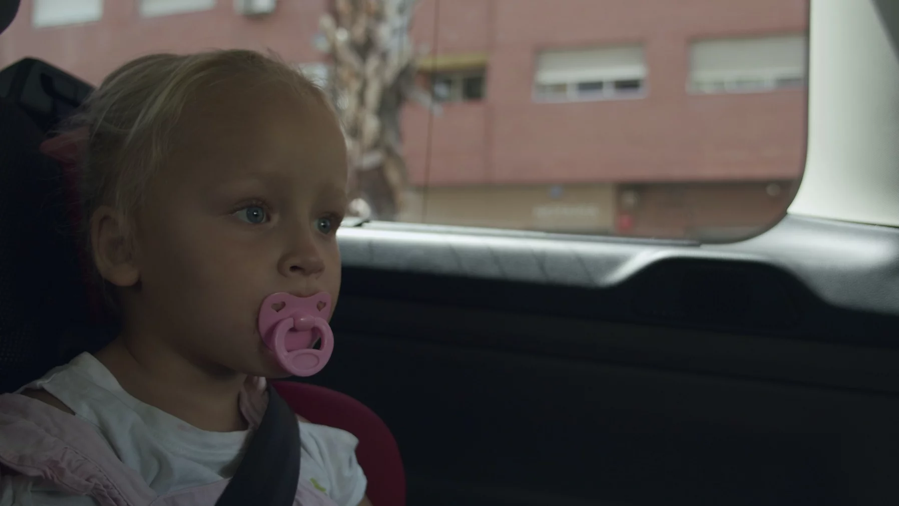 Wady zgryzu powstałe na skutek używania smoczka. Na zdjęciu dosyć duża dziewczynka siedzi w samochodzie ima smoczek.