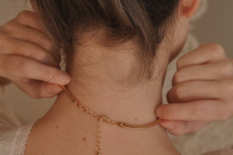 Kobieta zakładająca złoty naszyjnik, biżuteria