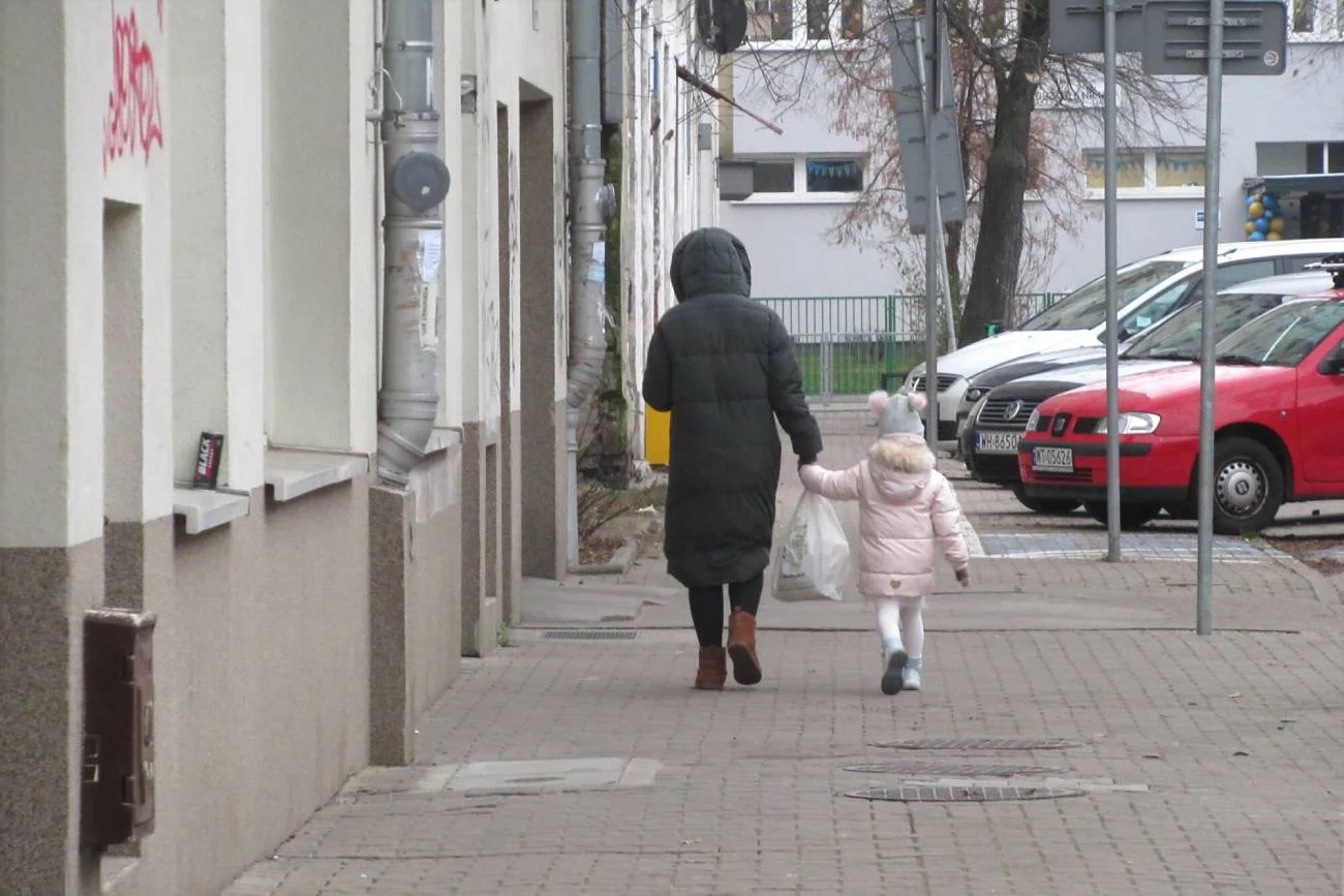 Kobieta idzie przez miasto z małym dzieckiem.