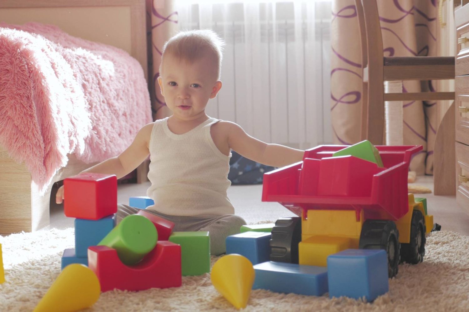 małe dziecko w wieku żłobkowym bawi sie na podłodze klockami