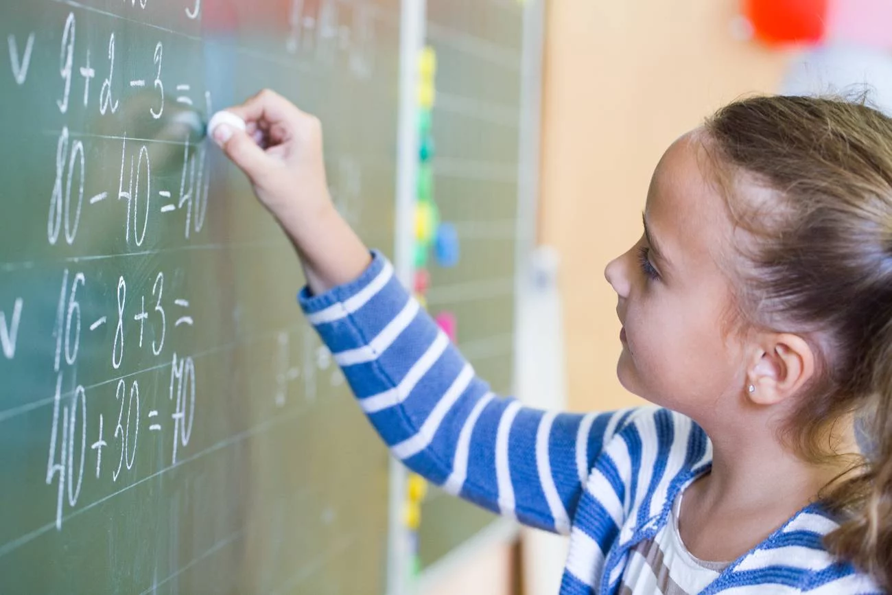Uczennica rozwiązuje zadania z matematyki na tablicy.