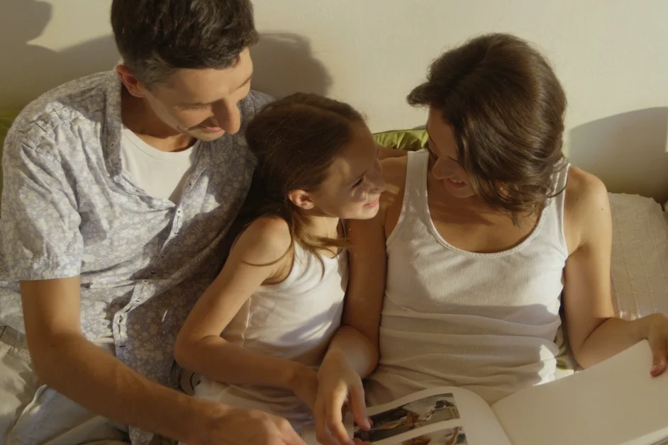 Na zdjęciu widać rodzinę - mama, tata i dziecko, którzy przeglądają album rodzinny.