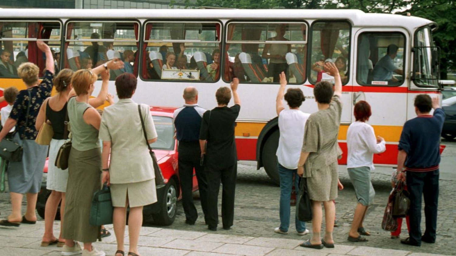 Rodzice żegnają autokar z dziećmi, który jedzie na kolonie.