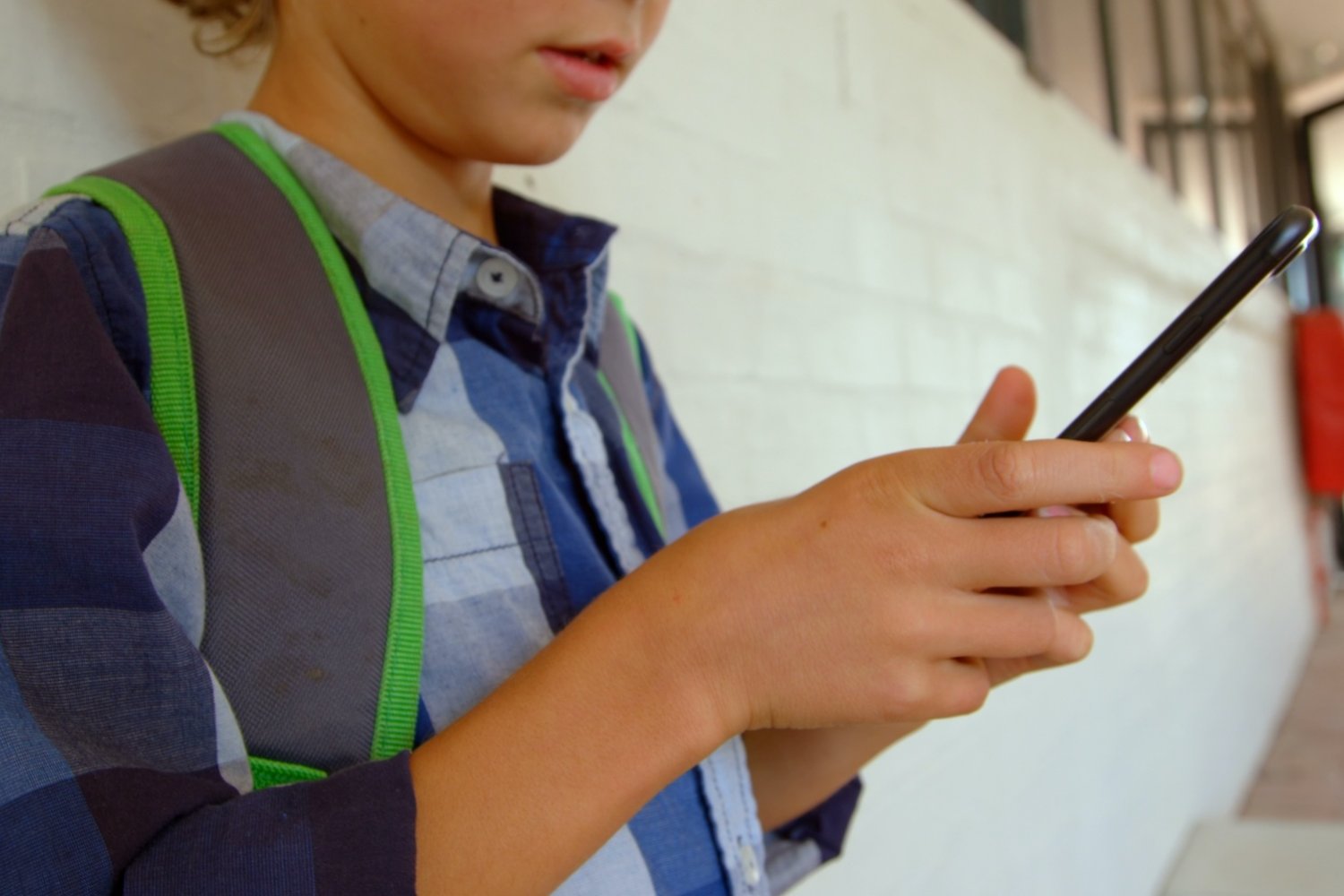 Dziecko siedzi na szkolnym korytarzu i patrzy w telefon