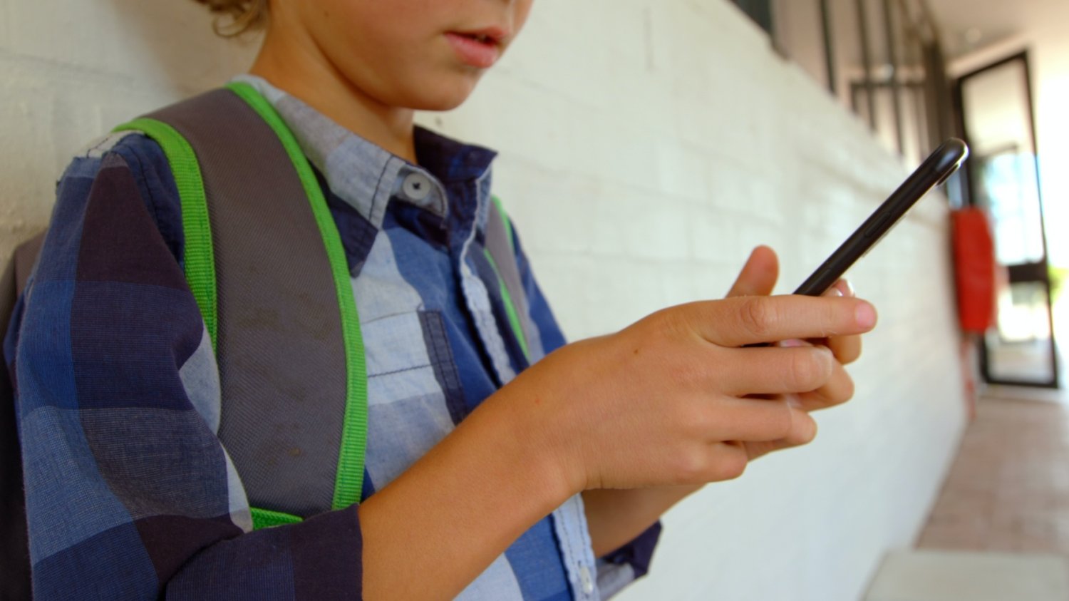 Czy nauczyciel może dziecku zabrać telefon? Dziecko siedzi na szkolnym korytarzu i patrzy w telefon