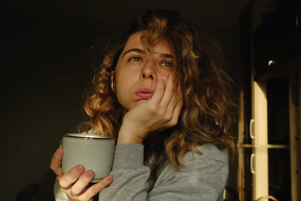 Prawdziwe życie kontra Instagram – nie wierzmy we wszystko, co tam pokazują. Na zdjęciu widać kobietę ze skrzywioną miną, zamyśloną z kubkiem czegoś do picia.