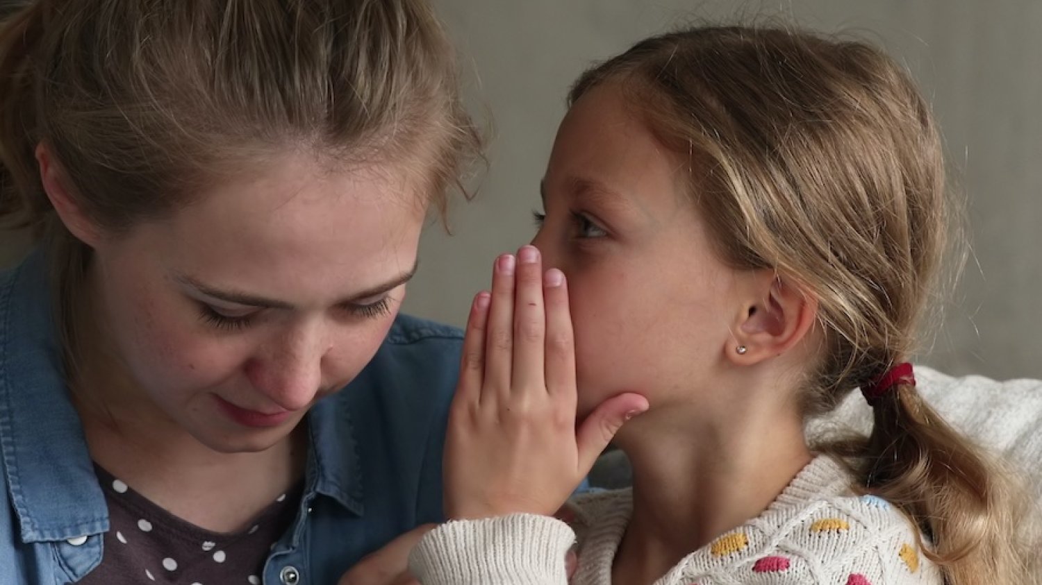 Jak rozmawiać z dzieckiem o wojnie. Na zdjęciu widać mamę i córkę, która z pewnym zawstydzeniem pyta o coś mamę. Wygląda na to, że jest to ważne pytanie.