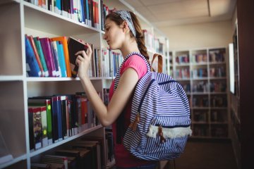 Nastolatka przegląda lektury w szkolnej bibliotece.