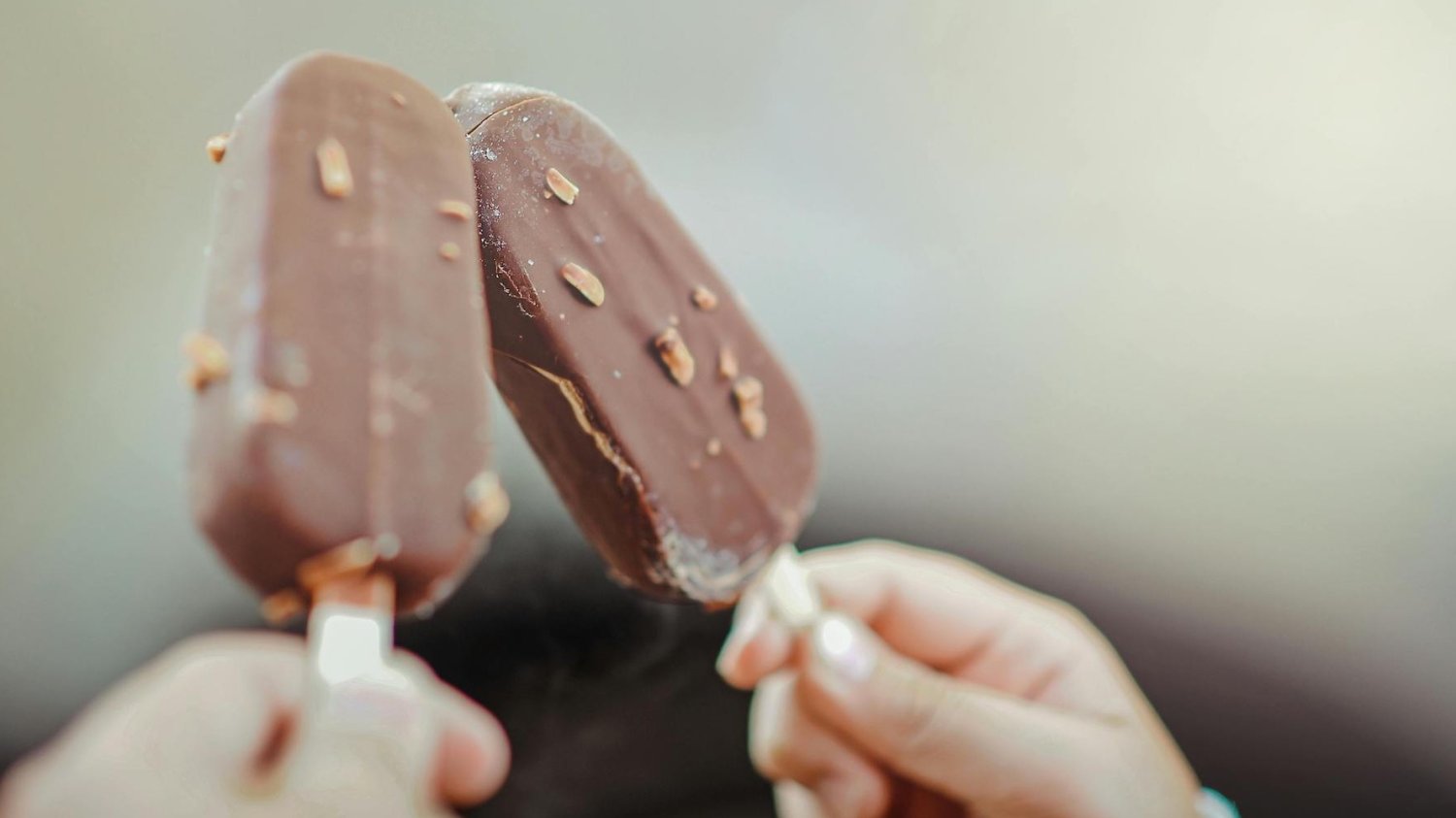 Na zdjęciu widać dwa lody na patyku w czekoladowej polewie.