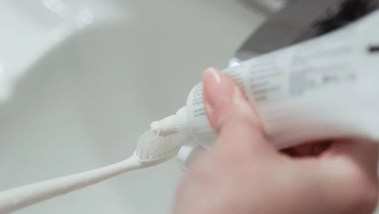 Na zdjęciu kobieta nakłada pastę na szczoteczkę.