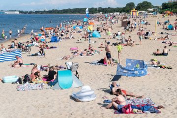 Rodziny z dziećmi odpoczywają na nadmorskiej plaży.