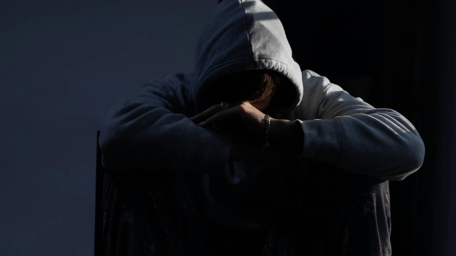 samotny chłopak, ofiara przemocy w kapturze na głowie chowa twarz między kolanami samotny chłopak, ofiara przemocy w kapturze na głowie chowa twarz między kolanami
