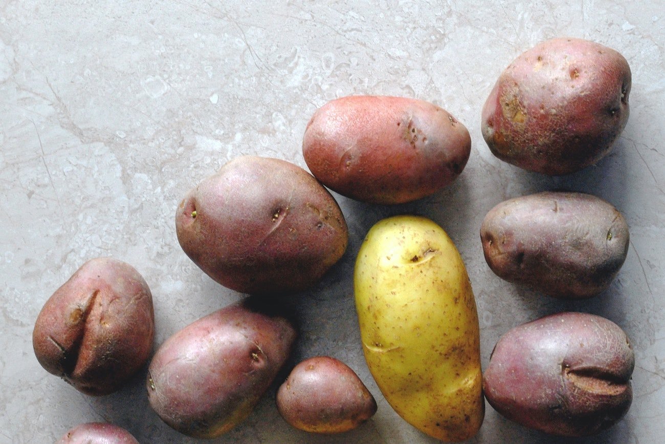 Ziemniaki fioletowe i jasne na białym, marmurowym tle.