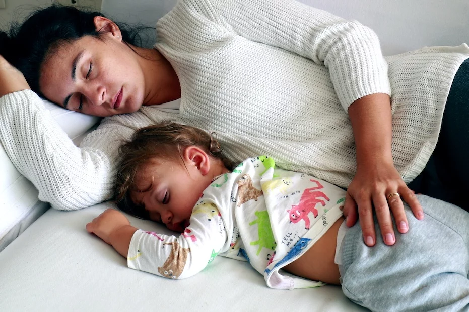 Na zdjęciu widać zmęczoną mamę, która usnęła z dzieckiem na kanapie.