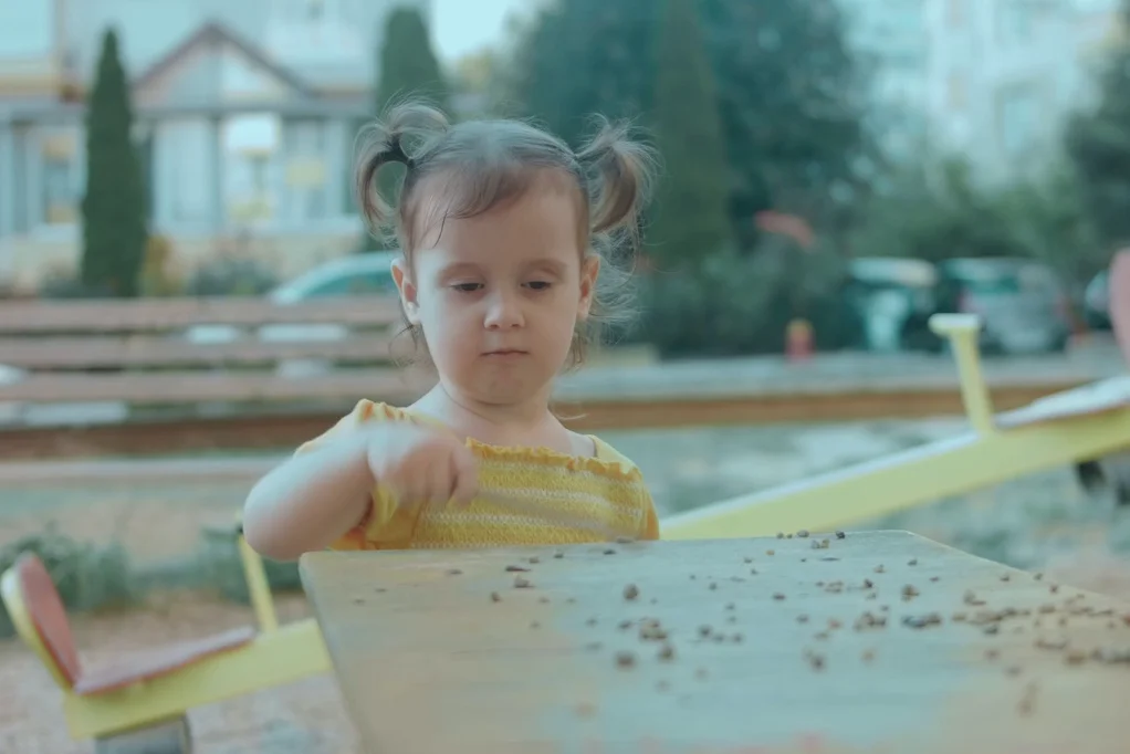 Na zdjęciu widać dziewczynkę na placu zabaw, w pobliżu piaskownicy.