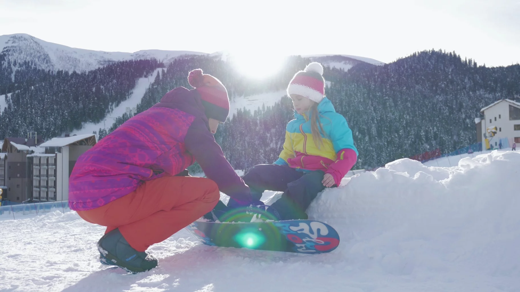 Koszt wyjazdu na narty w Polsce Na zdjęciu mama pomaga córce zapiąć deskę