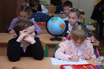 Dzieci siedzą w ławkach na lekcji w klasie.