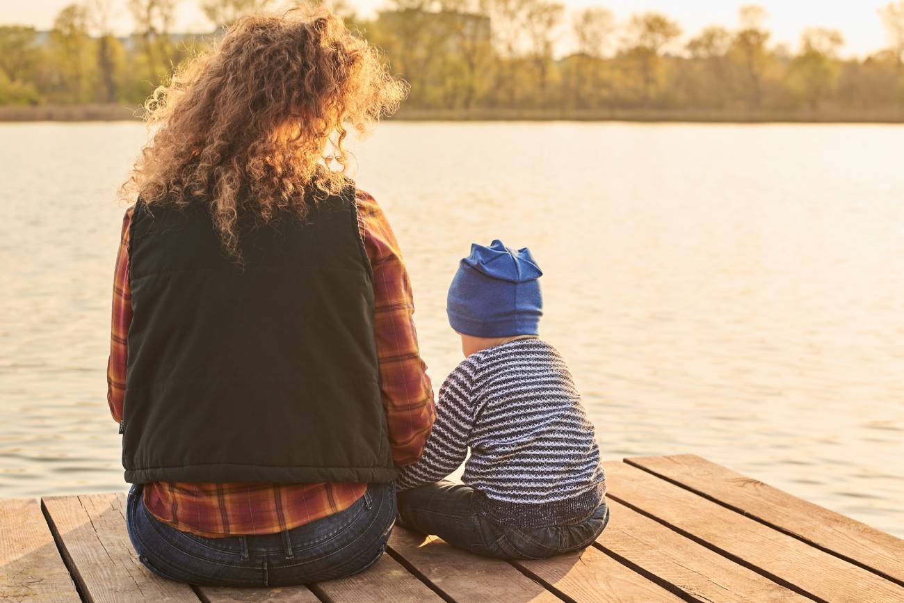 Małe dziecko z mamą siedzi nad wodą.