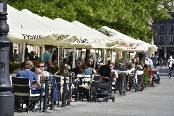 Restauracyjny ogródek, w którym przy stoliku siedzą rodzice z wózkiem.