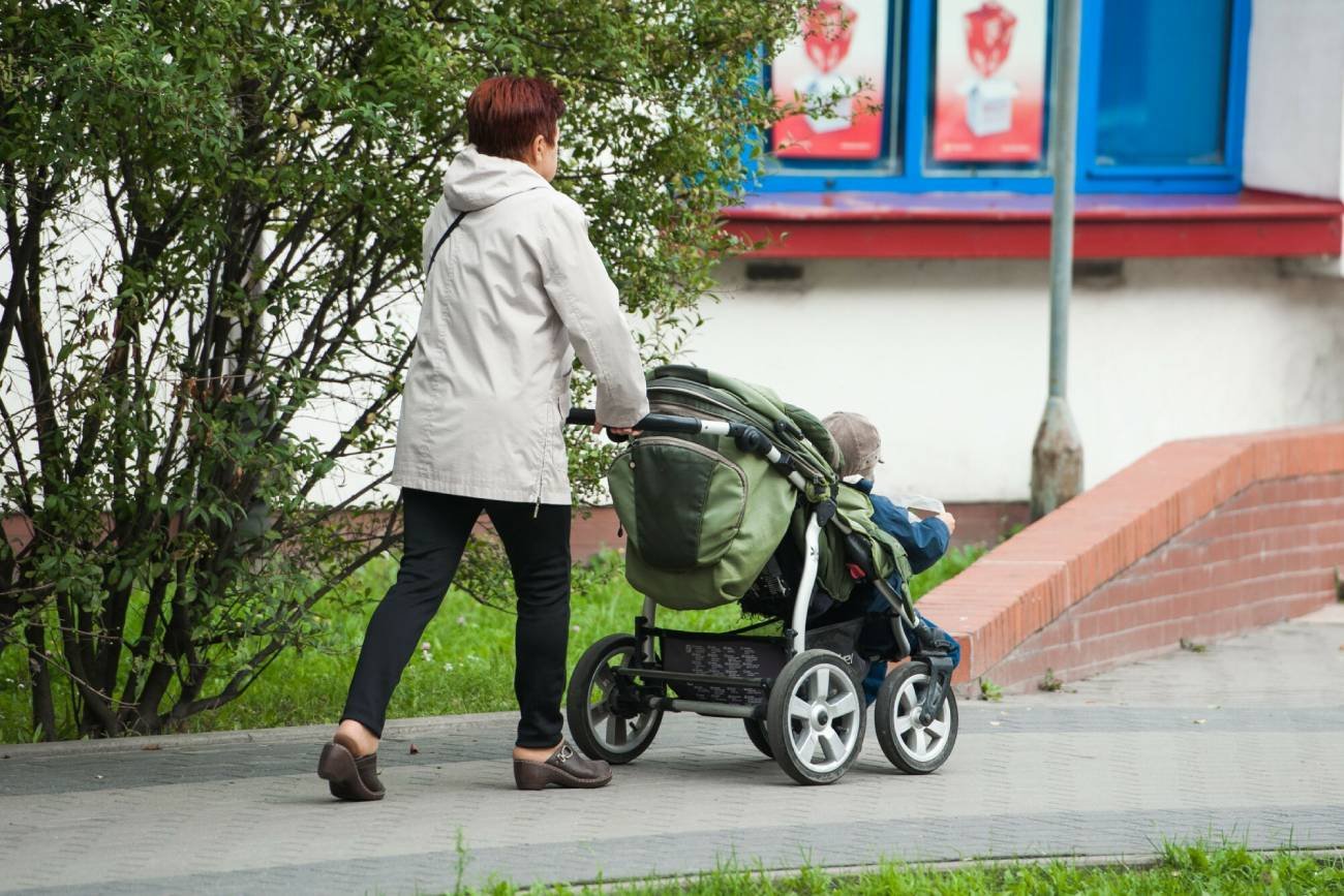 Babcia na spacerze, opiekująca się dzieckiem w wózku.