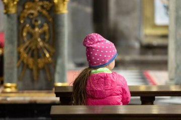 Kilkuletnia dziewczynka siedzi w kościele.