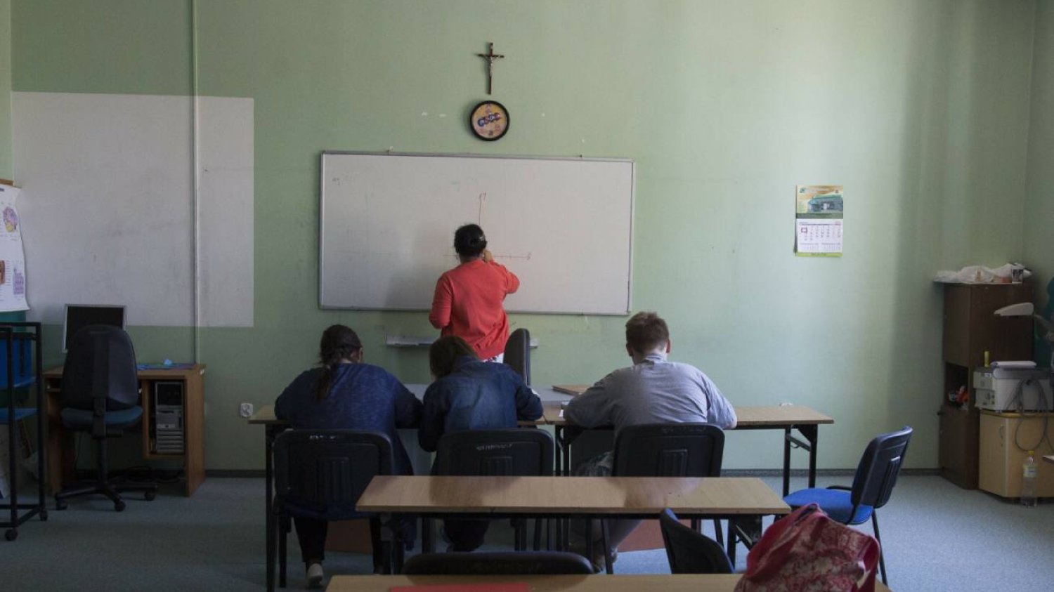 Lekcja w klasie z krzyżem na ścianie.