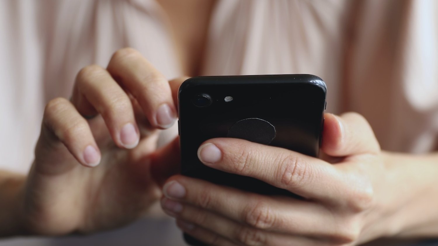 Na zdjęciu widać kobiecą rękę kobiety trzymającą telefon