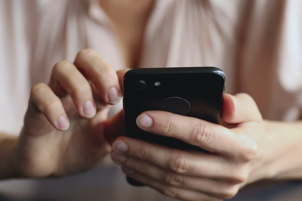 Na zdjęciu widać kobiecą rękę kobiety trzymającą telefon